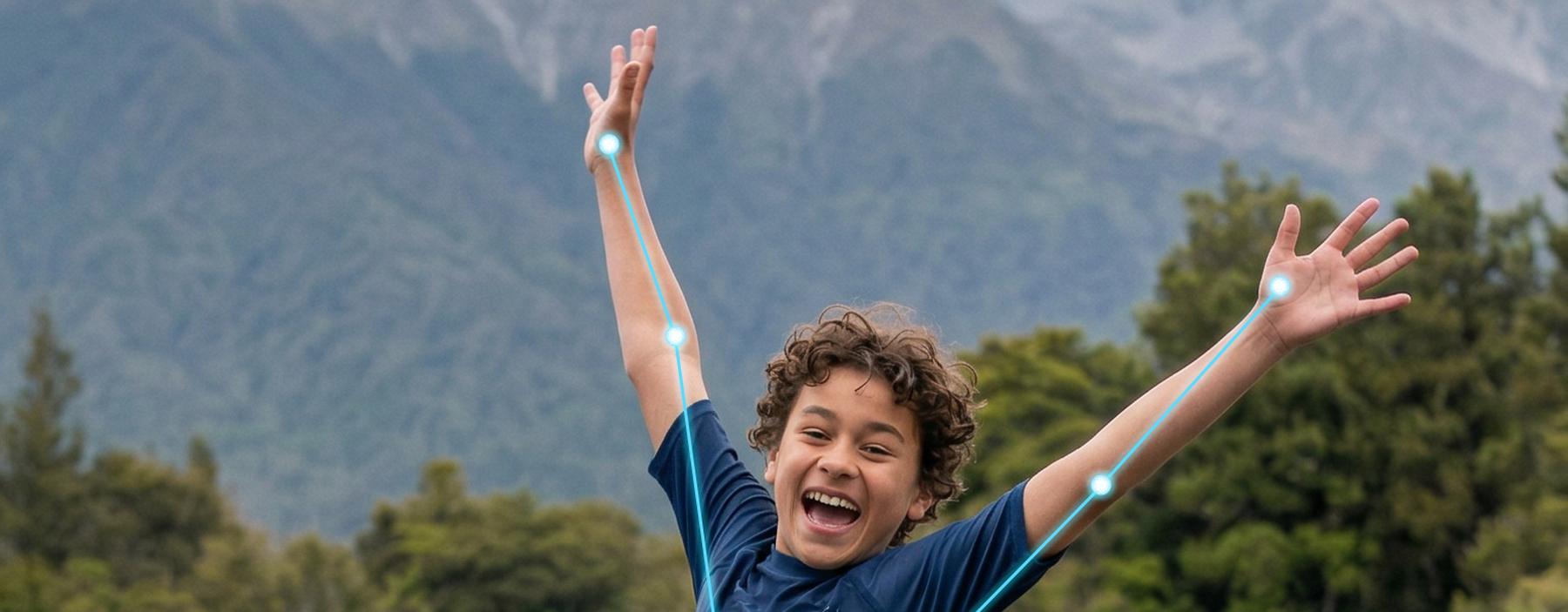 A child mid-leap with arms wide against the mountains.